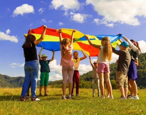 Children playing with a parachute silk in a field in the summer